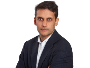 Lawyer posing confidently with arms crossed, wearing a dark blazer and white shirt against a neutral background.