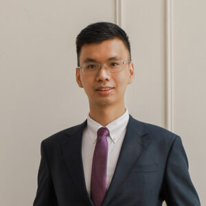 Lawyer in formal suit and glasses posing against a neutral backdrop in a professional setting.