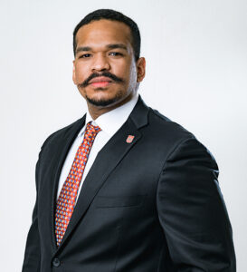 Lawyer in a formal suit with a tie, posing confidently against a neutral background.