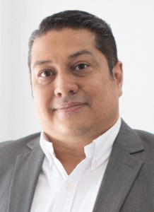 Lawyer In A Gray Suit With A White Shirt, Smiling, In A Professional Setting.