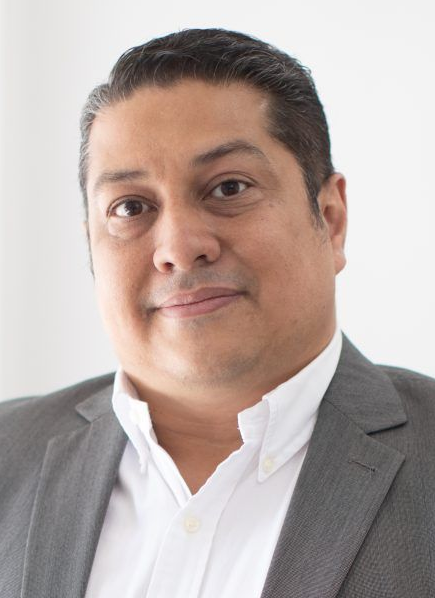 Lawyer In A Gray Suit With A White Shirt, Smiling, In A Professional Setting.