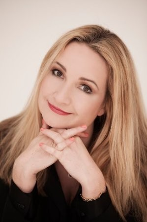 Lawyer with long blonde hair smiling and resting chin on hands, posed in a neutral setting.