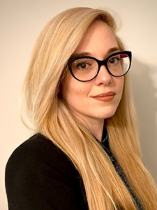 Legal professional with blonde hair and glasses, posing in a neutral setting, likely representing a law firm.