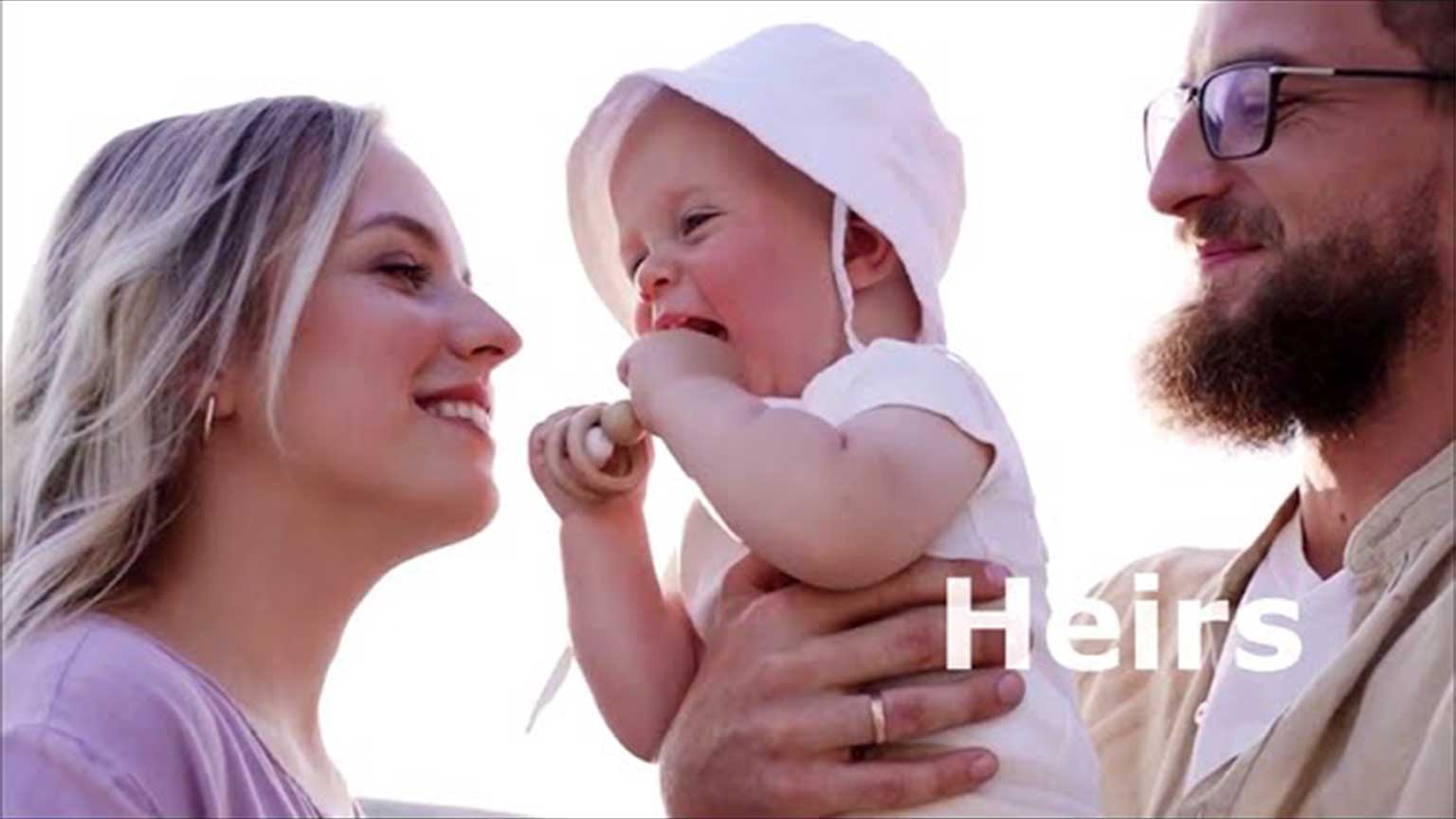 Family smiling together outdoors, with an infant held by a parent and playful interaction among them.