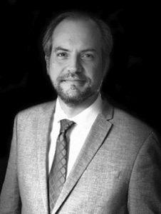 Lawyer in a suit, smiling against a plain background, presenting a professional demeanor.