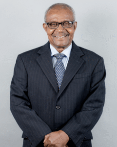 Lawyer smiling confidently in a suit, standing with arms crossed against a neutral background.