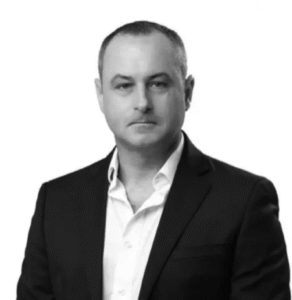 Lawyer in a black suit with white shirt, posing against a plain white background.