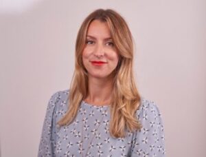 Legal professional with long blonde hair, wearing a patterned blouse, smiling against a neutral background.