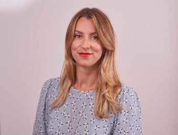 Legal professional with long blonde hair, wearing a patterned blouse, smiling against a neutral background.