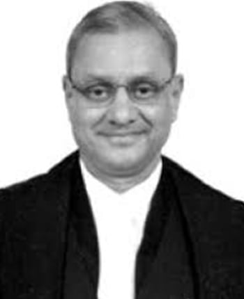 Judge in formal attire smiling with glasses, portrait against a neutral background.