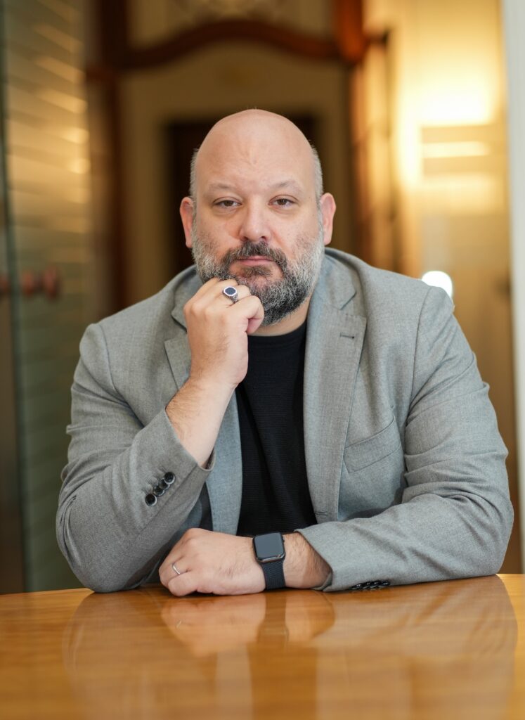 Lawyer sitting at a wooden table, resting chin on hand, in a professional office environment.