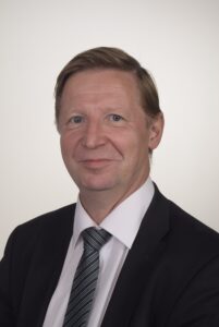 Lawyer In A Suit With A Tie, Posing For A Professional Headshot Against A Neutral Background.