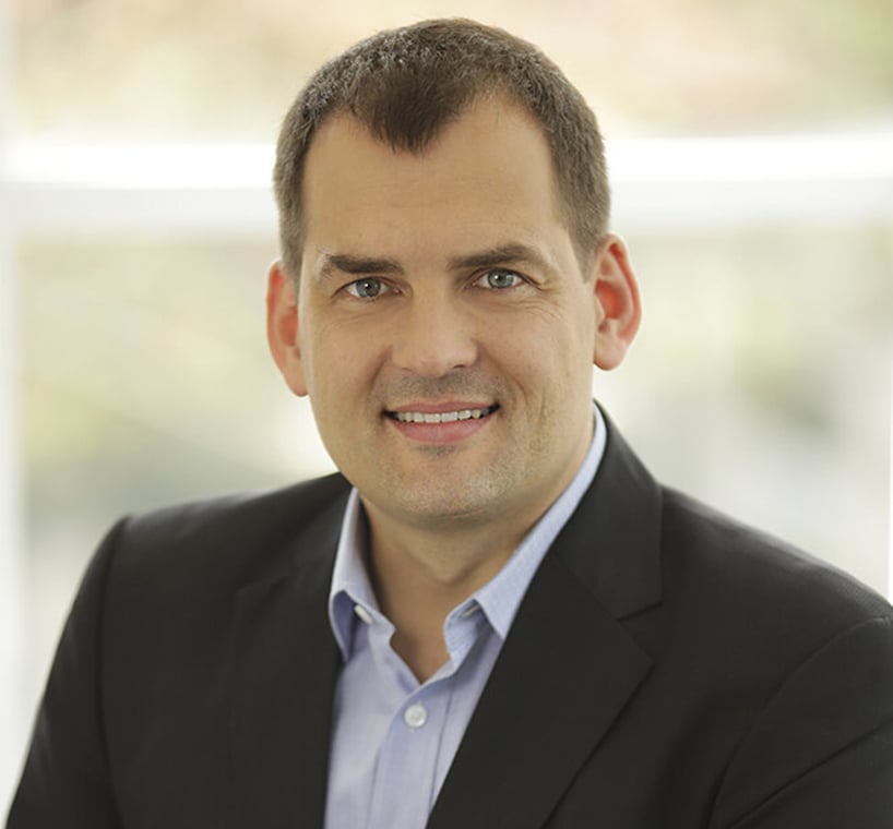Male professional smiling in a suit against a light background, likely a lawyer or attorney.