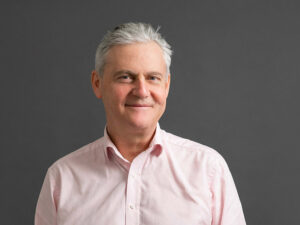 Legal professional smiling against a neutral background, presenting a approachable demeanor for client interactions.