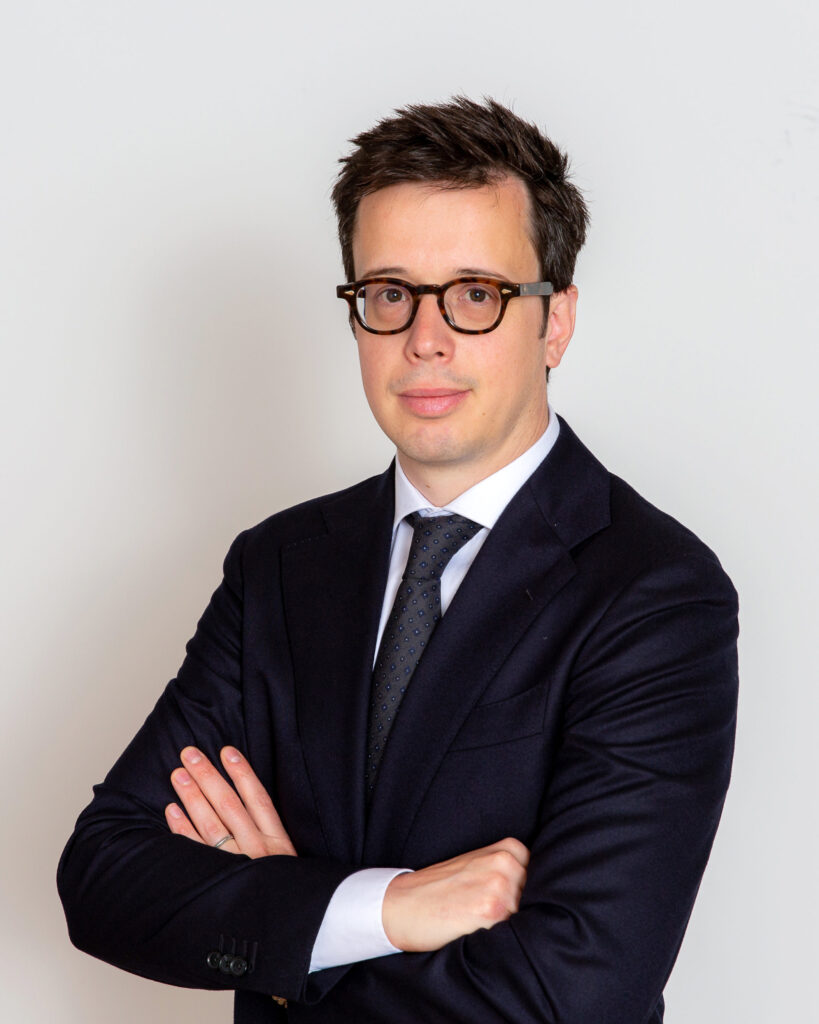 Attorney posing confidently with arms crossed, wearing a suit and glasses, against a plain background.
