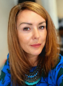 Professional woman with shoulder-length hair, wearing a blue patterned top and statement necklace, smiling at the camera.