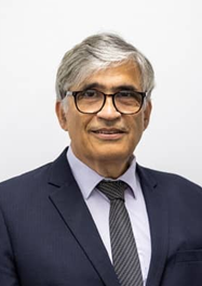 Professional man in a suit with glasses, smiling against a neutral background.
