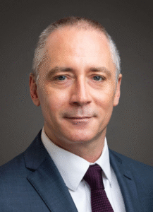 Male lawyer in a suit, professionally posed against a neutral background.