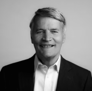 Corporate lawyer smiling at the camera, wearing a suit and collared shirt, set against a neutral background.