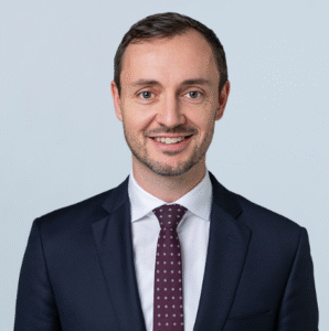 Smiling attorney in a dark suit with a patterned tie, posed against a light background.