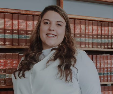 Lawyer smiling in front of a bookshelf filled with legal books in a law office setting.