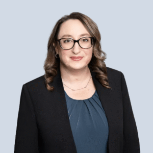 Female attorney in business attire, smiling, with shoulder-length hair, on neutral background.