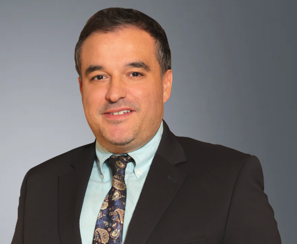 Lawyer in a suit with a patterned tie, smiling against a neutral background.