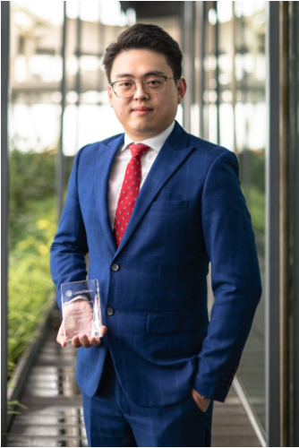 Legal professional holding an award in a business suit, standing in a modern office environment with glass walls.