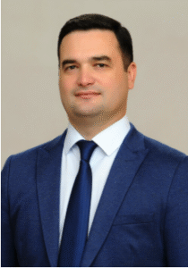 Professional man in a blue suit and tie, presenting a confident demeanor against a neutral background.