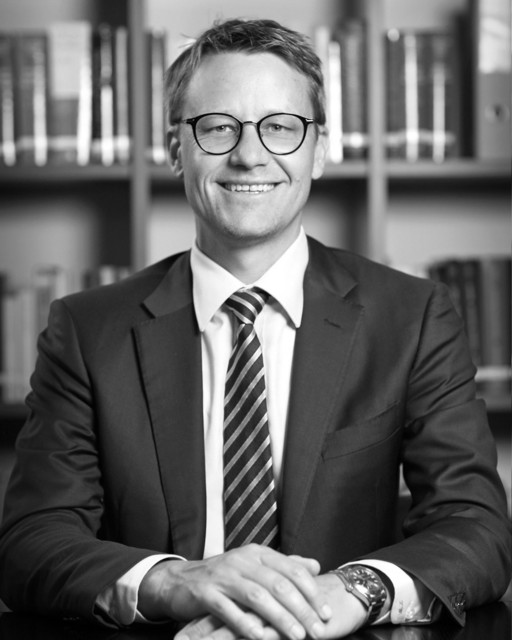 Lawyer smiling confidently at desk in front of bookshelves filled with legal texts.