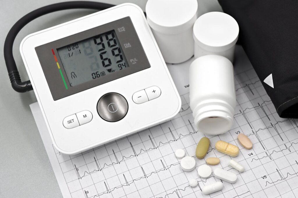 Blood pressure monitor on ECG paper with assorted medication capsules and tablets scattered around.