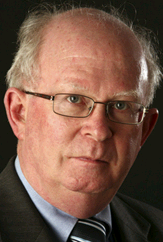 Legal professional with glasses and a serious expression, dressed in a suit against a dark background.