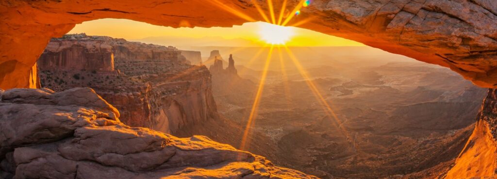 Sunset illuminating canyon landscape viewed through natural rock archway.