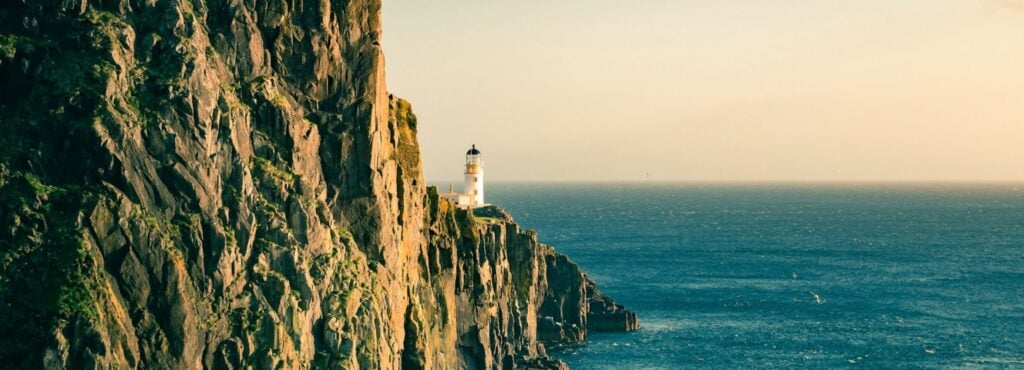 Coastal cliff with lighthouse overlooking the ocean at sunset.