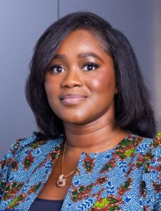 Professional woman with dark hair, wearing a patterned outfit, in an office setting.