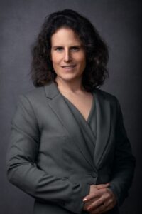 Lawyer in a gray suit posing confidently against a neutral backdrop.