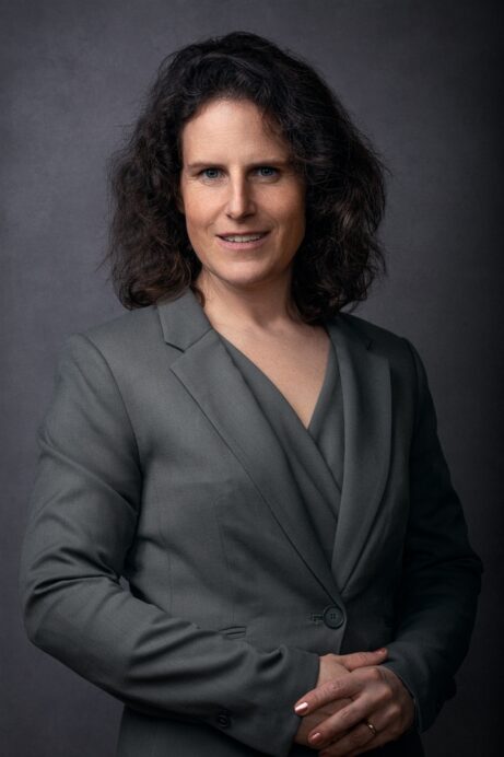 Lawyer in a gray suit posing confidently against a neutral backdrop.