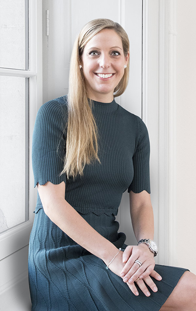 Legal professional smiling while seated by a window, dressed in a dark outfit, in a modern office setting.