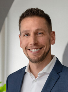 Male lawyer smiling in a professional setting, wearing a suit and shirt, with neutral background lighting.