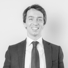 Professional man in a suit smiling against a neutral background, possibly representing legal expertise.
