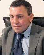 Lawyer seated and focused, wearing a suit, in a professional office setting.