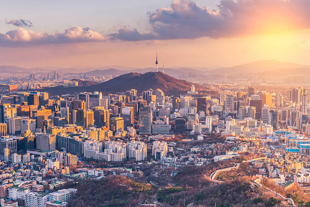 Cityscape of Seoul at sunset with modern buildings and Namsan Tower on the mountain in the background.