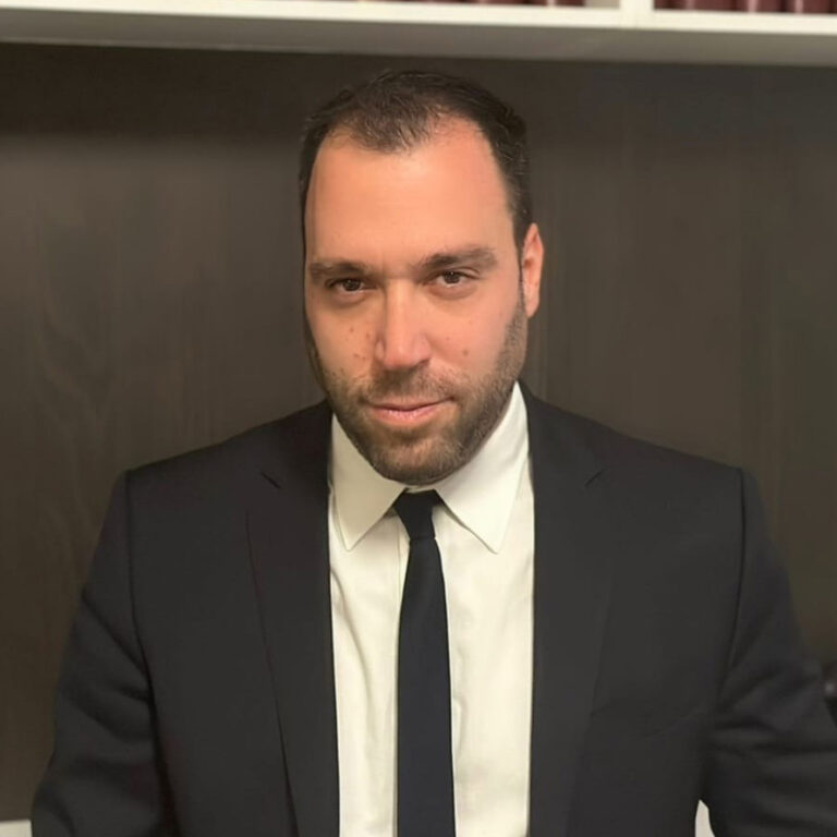 Lawyer in a suit, posing with a serious expression, in front of dark wooden shelves.