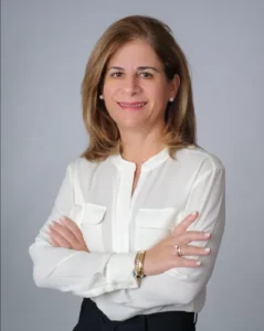 Lawyer posing with arms crossed, smiling, wearing a white blouse in a professional portrait setting.