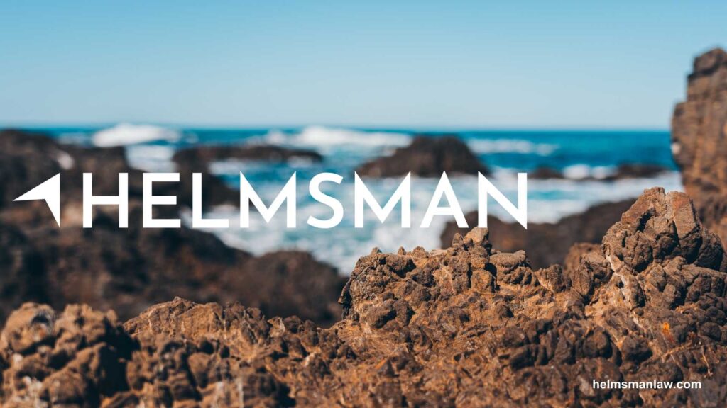 Text logo with "HELMSMAN" on rocky beach with ocean waves in the background.