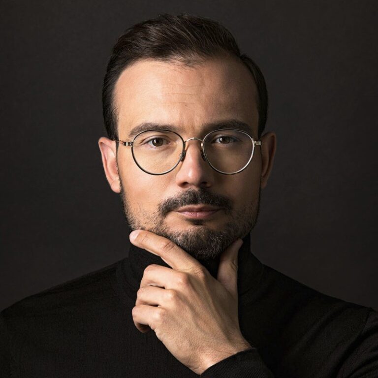 Male professional with glasses thoughtfully posing in front of a dark background.