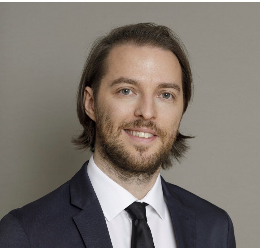 Lawyer in a suit smiling against a neutral background, representing a professional legal setting.