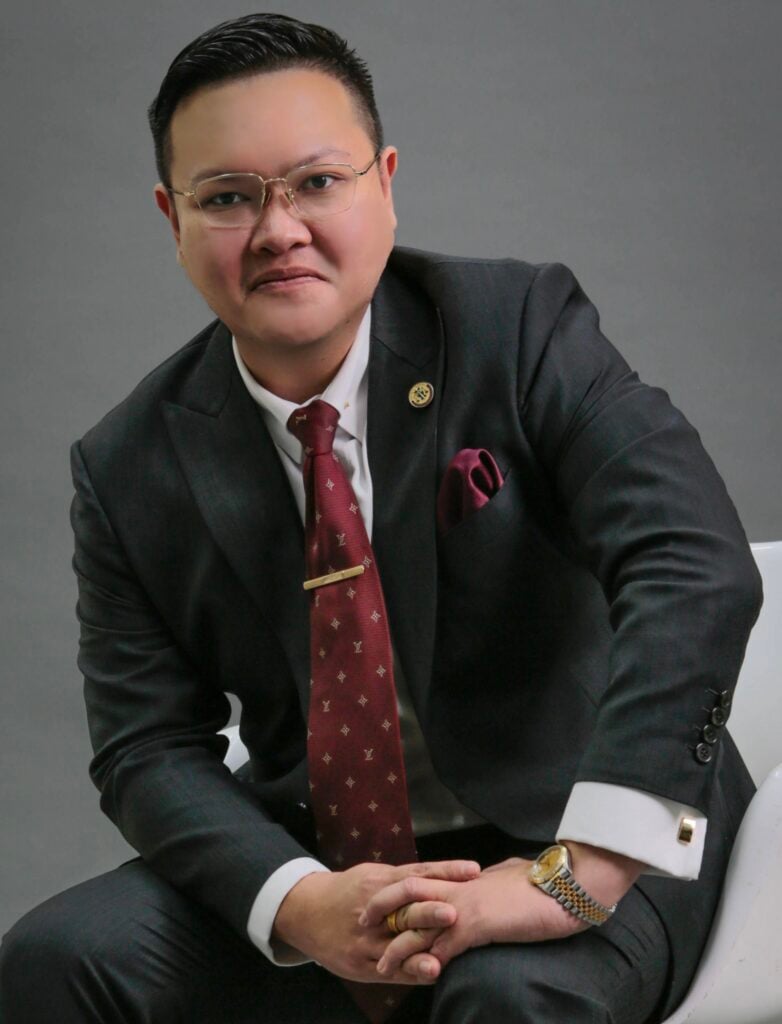Lawyer in a black suit with glasses, seated and looking at the camera in a professional setting.