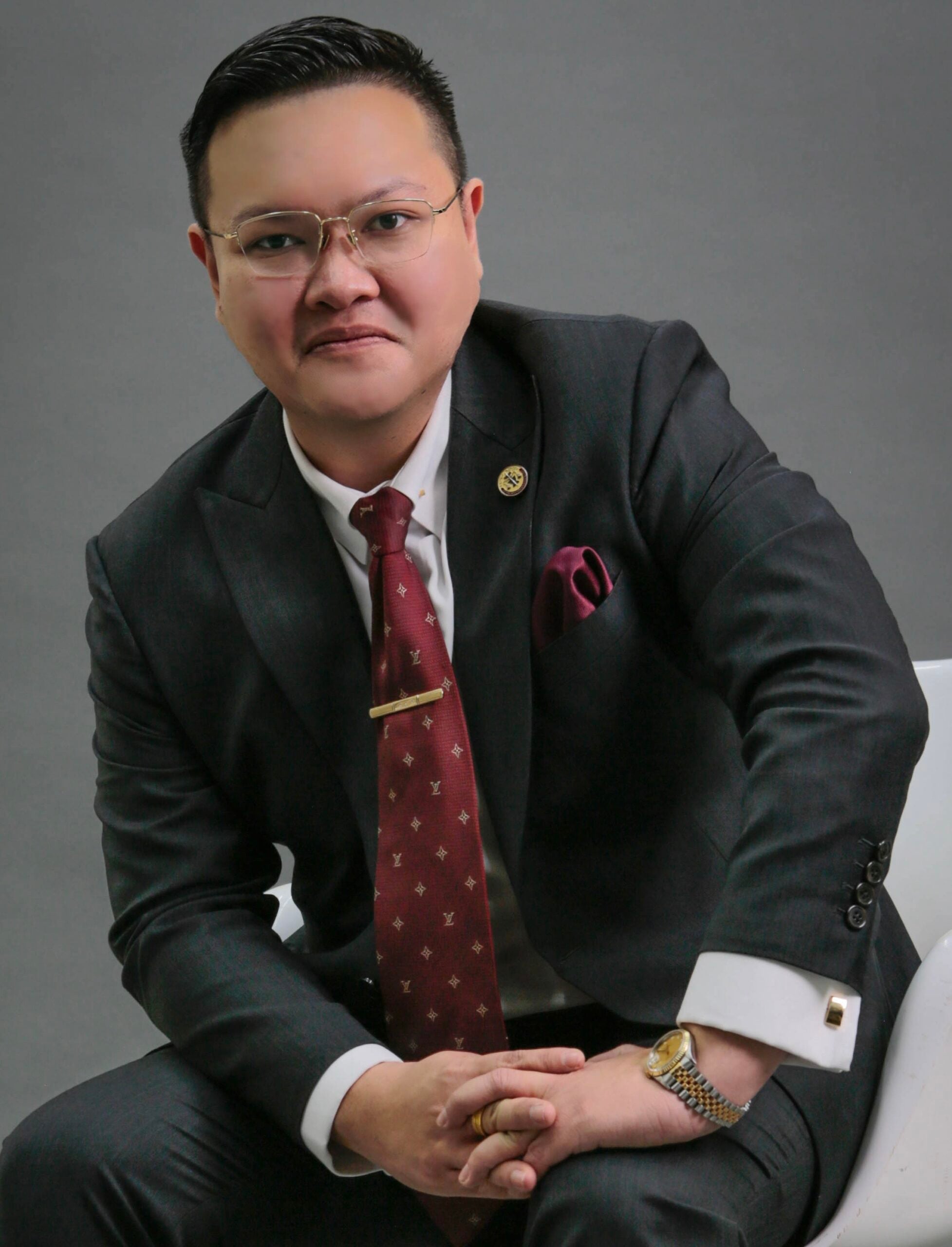 Lawyer in a black suit with glasses, seated and looking at the camera in a professional setting.