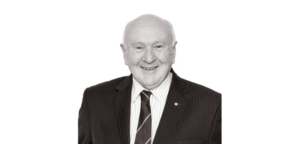 Senior lawyer smiling, wearing a striped suit and tie, against a plain background.